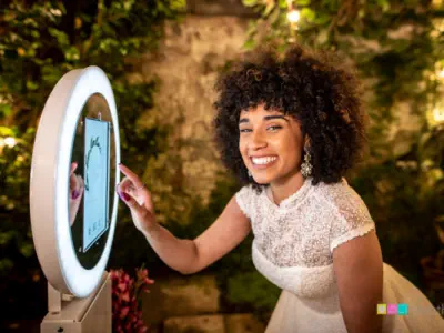 A smiling bride in a white lace dress interacts with a circular selfie station at an outdoor night-time event. Surrounding greenery and soft lighting create a warm atmosphere, perfect for those considering luxury photo booth hire in Oxfordshire